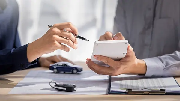 insurance car lease two people sharing numbers on a calculator with keys on table